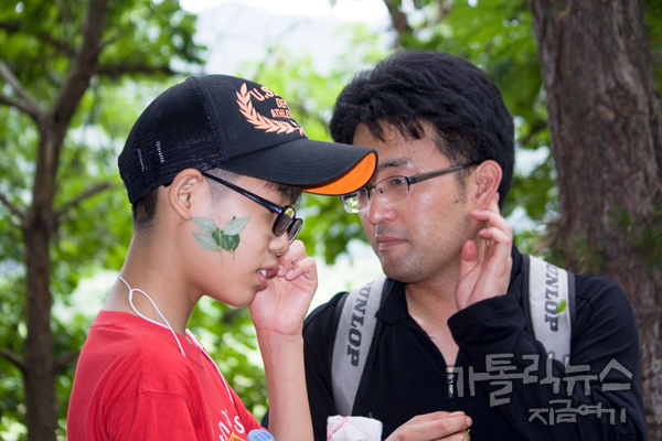 산초나무 잎을 화장하듯이 볼에 문지르는 아이와 신부님.