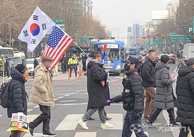 지난 2월 15일, 광화문 광장 횡단보도를 건너고 있는 극우 집회 참가자가 태극기와 성조기를 들고 있다. ⓒ왕기리 기자