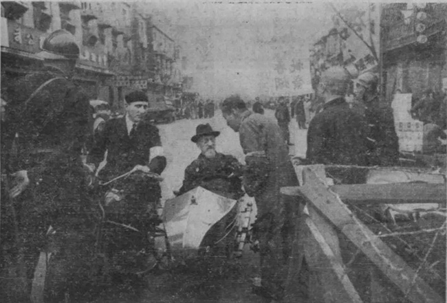 1937년 11월 15일 자퀴노 신부의 모습. 사이드카에 탄 채 누군가와 이야기하고 있다. 사진에 나오는 거리는 ‘난민 안전 구역’ 경계인 인민로(人民路)이다. 자퀴노 주위에 있는 사람들은 프랑스 조계 출입구 관리 인원과 경계병인 것 같다. (사진&nbsp;출처 = <u>pastvu.com)</u><br>