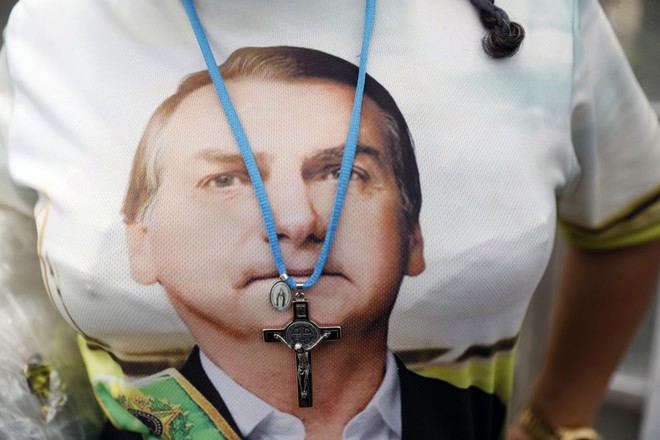 2019년 1월 1일 브라질 브라질리아에서 자이르 보우소나루 대통령 취임식을 앞두고, 그의 얼굴이 인쇄된&nbsp;윗옷 위에 십자가 목걸이를 착용한 지지자의 모습. ©AP, 실비아 이즈키에르두<br>